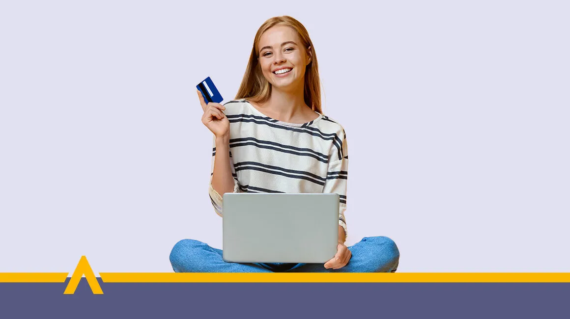 Uśmiechnięta młoda kobieta siedząca z laptopem i kartą płatniczą w ręce