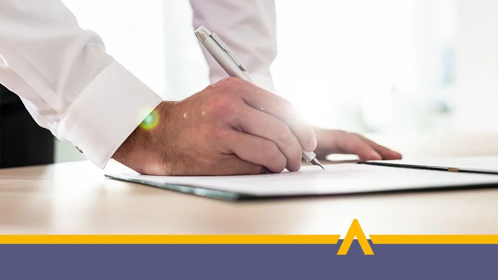 Mężczyzna w jasnej koszulce podpisujący oświadczenie przy biurku