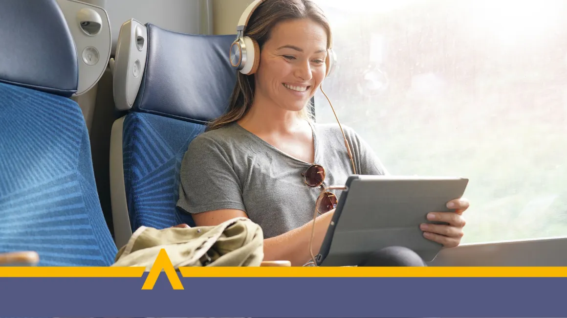 Uśmiechnięta kobieta w słuchawkach korzystająca z tabletu w pociągu