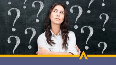 Kobieta zastanawiająca się na tle tablicy z narysowanymi znakami zapytania, symbolizująca wątpliwość lub potrzebę podjęcia decyzji finansowej.